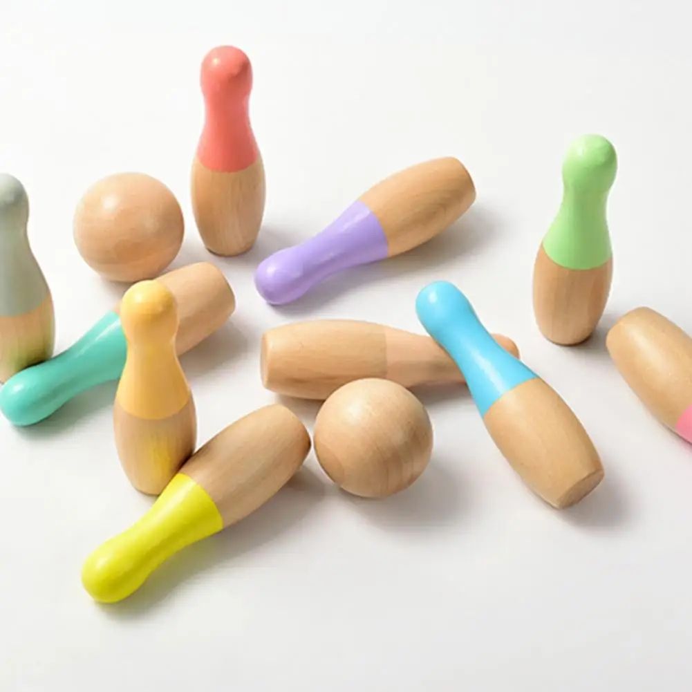 A collection of InvenToy Montessori Bowling Set wooden toy pins scattered on a white background, with various pins featuring colored caps in pink, green, purple, blue, and yellow.