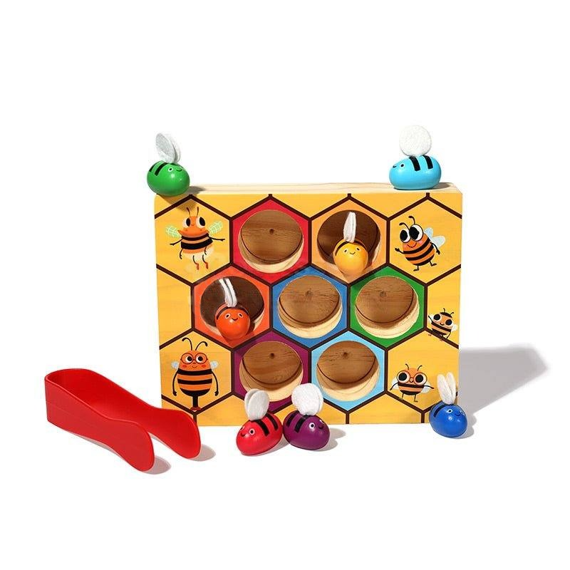 A colorful InvenToy Montessori Bee Box featuring hexagonal slots and cartoon bee illustrations, with wooden bee pieces in various colors positioned on and around the board.