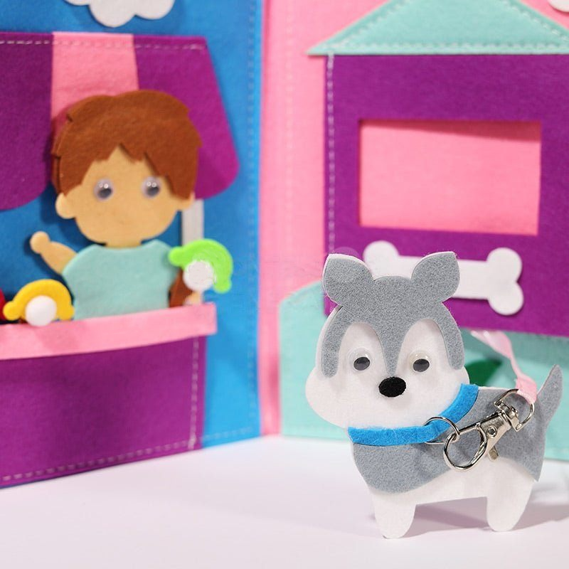 A InvenToy Montessori Story Book display featuring a small boy figure in a blue shirt inside a pink and purple house, and a gray and white dog with a blue collar standing outside.