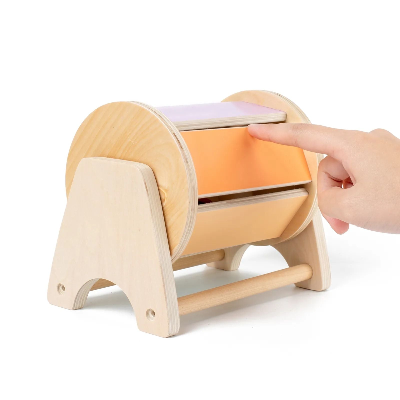A hand pressing a button on a wooden InvenToy Montessori Spinning Drum baby toy, on a white background.