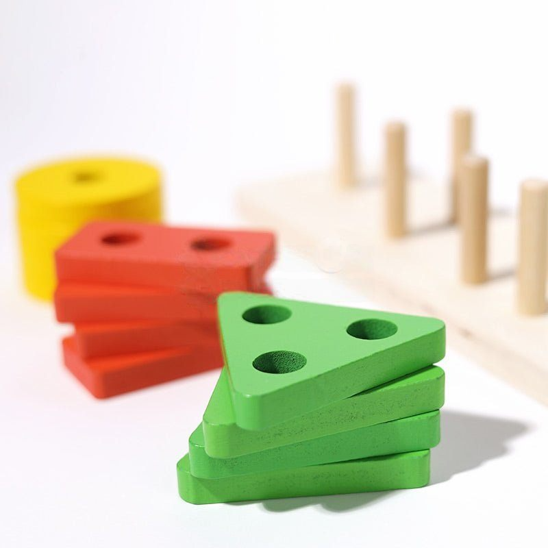 Colorful wooden Montessori Building Blocks with pegs in a spacious play area, showcasing a green triangle, red parallelogram, and yellow circle, focused on developmental learning and motor skills by InvenToy.