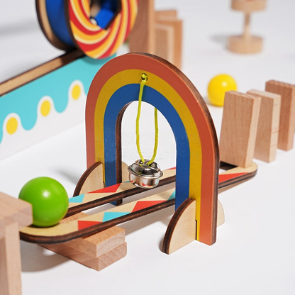 InvenToy Montessori Domino Run set featuring a rainbow arch with a hanging bell, balls, and a slide, all on a white background with playful geometric elements.