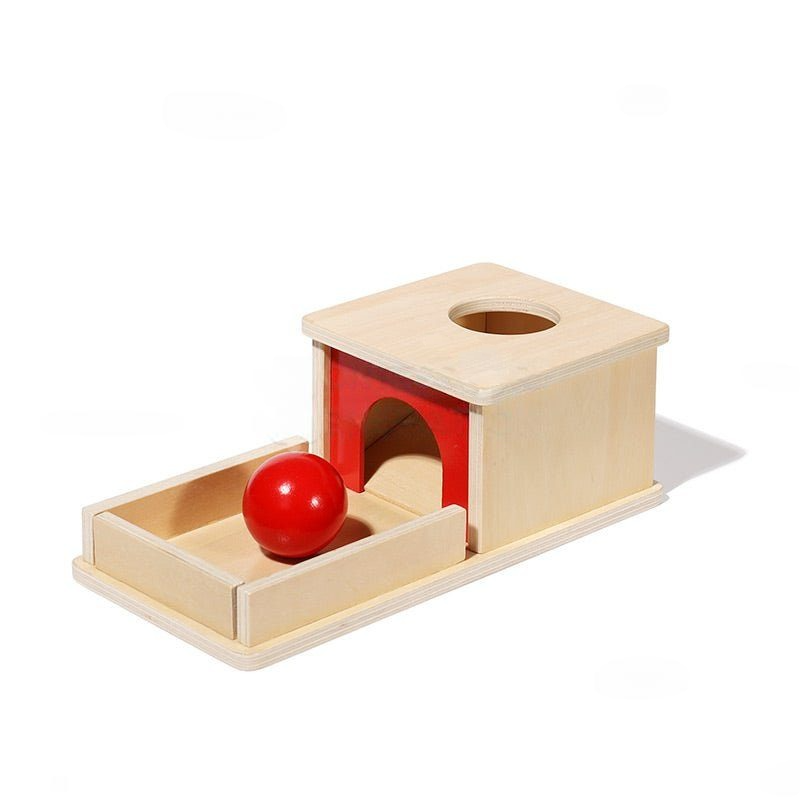 A wooden InvenToy Montessori Object Permanence Box featuring a house-shaped block with a round hole and a red ball beside it, set against a white background.