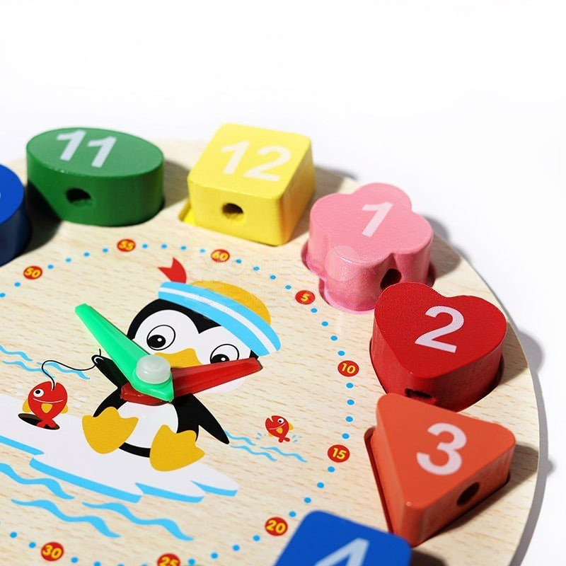 An educational InvenToy Montessori Penguin's Clock featuring a colorful wooden clock with numbers, a small pegged penguin in the center holding a fishing rod, and various fish shapes around the perimeter.