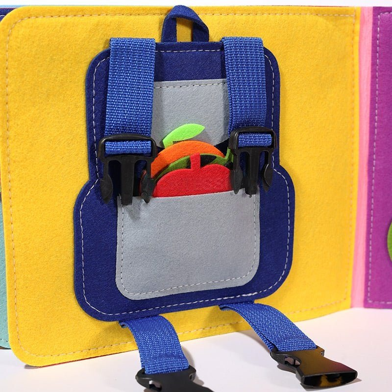 A colorful felt children's backpack featuring a blue and grey design with Montessori Story Book shaped like an apple and carrot poking out, displayed against a multicolored backdrop by InvenToy.