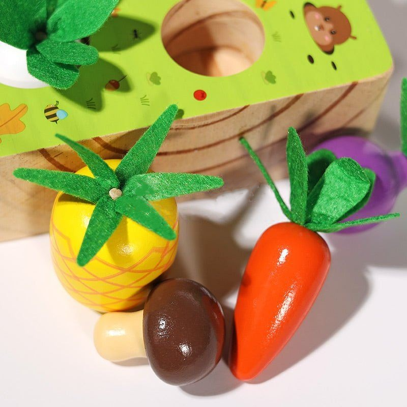 Wooden Montessori Vegetable Set including a carrot with green felt top, a pineapple with textured sides, and a kiwi, displayed with a partial view of an InvenToy game featuring fruit shapes.