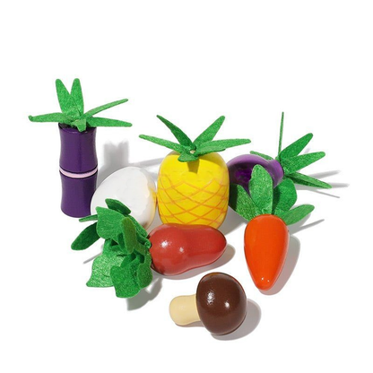 Colorful InvenToy Montessori Vegetable Set arranged on a white background, including a pineapple, eggplant, carrots, and a mushroom, all featuring stylized green felt leaves.