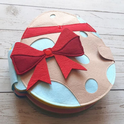 A colorful round fabric pouch with a beige base, decorated with blue polka dots and red lines featuring a prominent red bow on top, perfect as an InvenToy storage option for the Montessori Rabbit's Book.