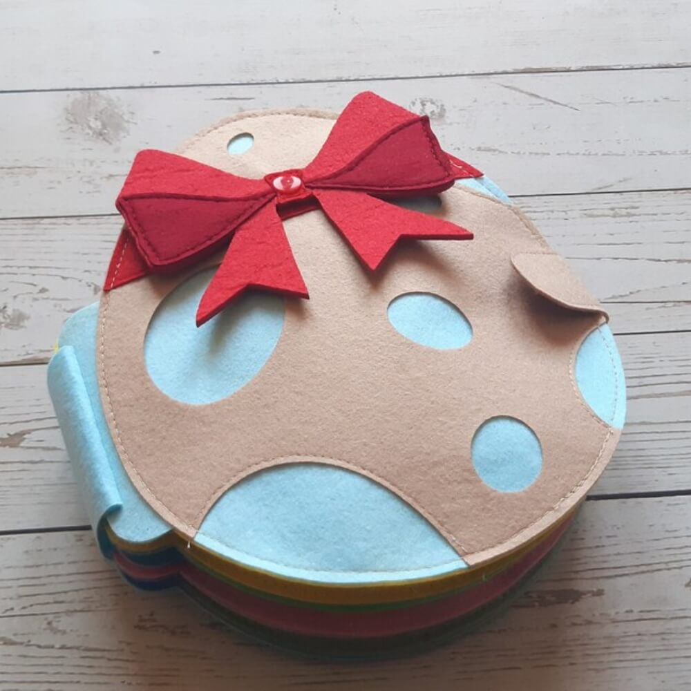 A handmade felt box designed to look like a whimsical cookie, with a tan base, blue and tan polka dots, and a bright red bow on top, perfect as InvenToy's Montessori Rabbit's Book.
