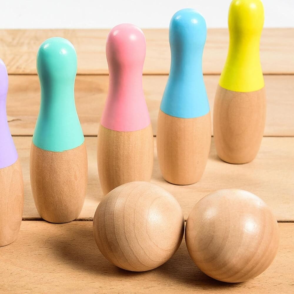 Colorful wooden bowling pins and balls set on a wooden surface, featuring InvenToy Montessori Bowling Set in various pastel colors with a natural wood lower half.