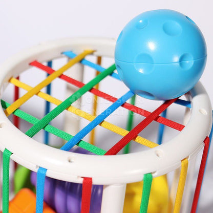 A close-up of a colorful InvenToy Montessori Shape Blocks with a blue ball on a multicolored elastic band framework enclosed in a white round ring.