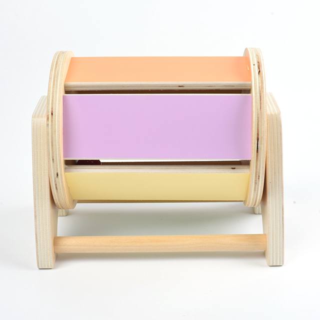 A wooden InvenToy Montessori Spinning Drum with three colored drawers: orange, purple, and yellow, against a white background.